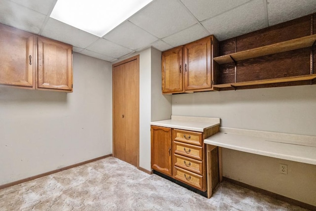 unfurnished office featuring baseboards, light carpet, built in desk, and a paneled ceiling