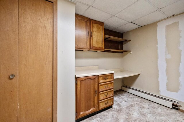 unfurnished office featuring a baseboard heating unit, built in desk, and a drop ceiling