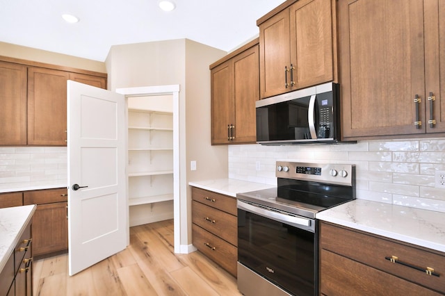 1504 14th Ave NE, Kasson, MN 55944 - kitchen with stainless steel appliances, light wood-style flooring, light stone counters, backsplash, and brown cabinets