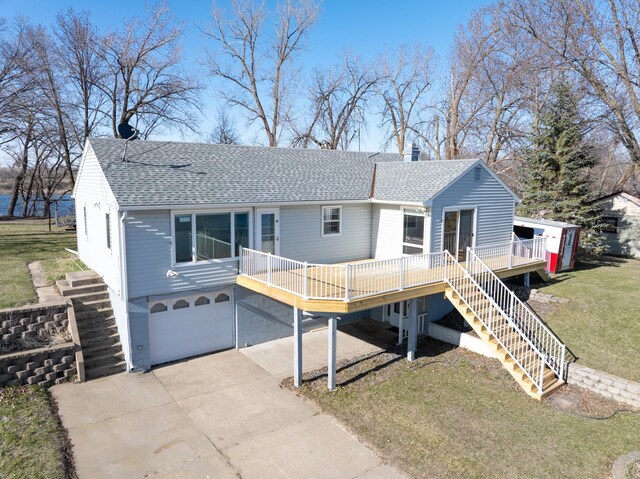 rear view of property with a deck, roof with shingles, stairs, and a garage