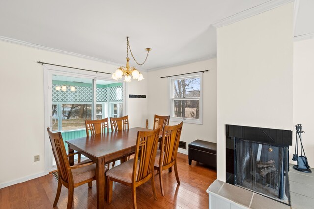 dining area with baseboards, an inviting chandelier, wood finished floors, a multi sided fireplace, and crown molding