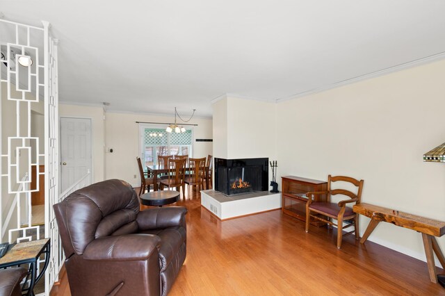 living area featuring light wood-type flooring, baseboards, an inviting chandelier, a multi sided fireplace, and ornamental molding