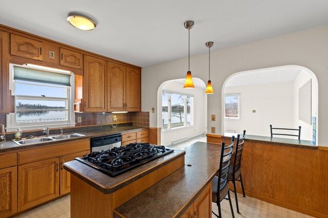 kitchen featuring dark countertops, a sink, arched walkways, and dishwashing machine