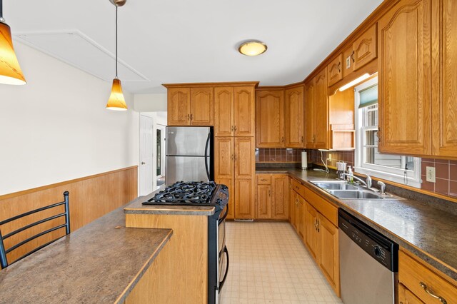 kitchen with stainless steel appliances, light floors, dark countertops, a sink, and brown cabinetry