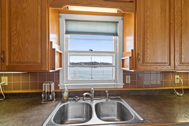 kitchen with brown cabinets, dark countertops, tasteful backsplash, and a sink