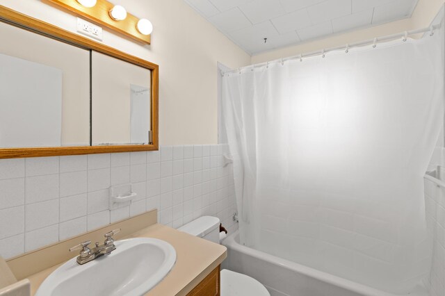 bathroom with wainscoting, vanity, tile walls, shower / tub combo, and toilet