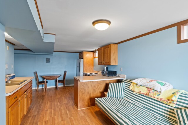 kitchen with a sink, light wood-type flooring, light countertops, a peninsula, and freestanding refrigerator