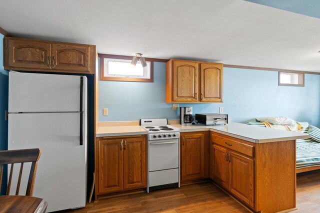 kitchen featuring a peninsula, wood finished floors, white appliances, brown cabinets, and light countertops