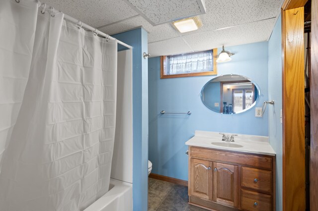 full bath featuring toilet, vanity, baseboards, a paneled ceiling, and shower / tub combo