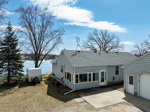 rear view of house featuring a shingled roof, central AC unit, and a water view