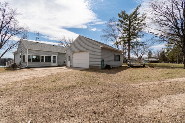 rear view of property featuring a garage, dirt driveway, and roof with shingles