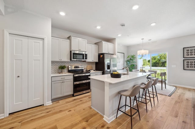 kitchen with light countertops, light wood-type flooring, a kitchen island with sink, a kitchen bar, and appliances with stainless steel finishes