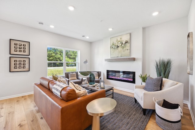 living area with baseboards, a glass covered fireplace, light wood-style floors, and recessed lighting