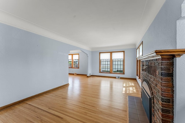 unfurnished living room featuring light wood-style floors, a fireplace with flush hearth, arched walkways, baseboards, and crown molding