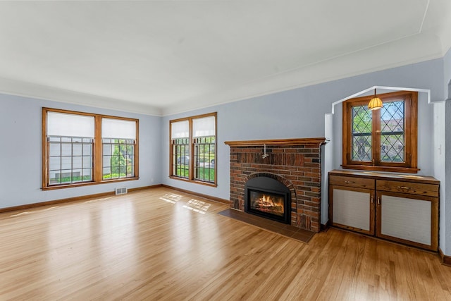 unfurnished living room featuring light wood-style flooring, a fireplace, crown molding, and baseboards