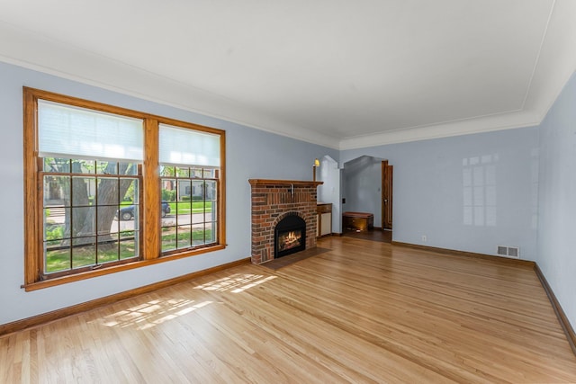 unfurnished living room featuring light wood-style flooring, baseboards, crown molding, and a brick fireplace