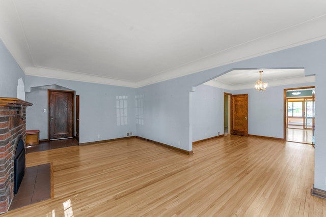 unfurnished living room with a fireplace, a chandelier, light wood-style flooring, ornamental molding, and baseboards