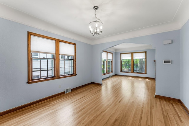 spare room featuring arched walkways, a chandelier, baseboards, and light wood-style floors