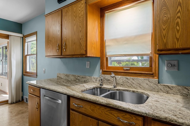 kitchen with dishwasher, brown cabinetry, a sink, and light stone countertops