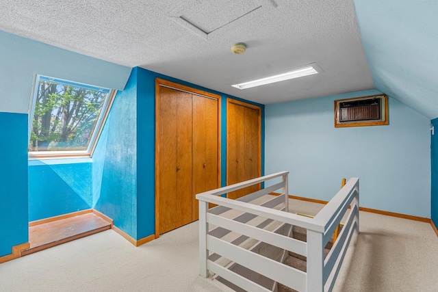 carpeted bedroom featuring vaulted ceiling, a wall mounted air conditioner, baseboards, two closets, and a textured ceiling