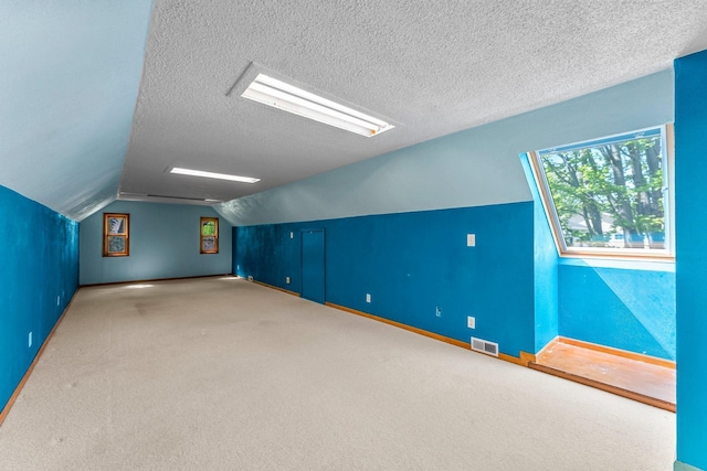 additional living space featuring vaulted ceiling, a textured ceiling, baseboards, and carpet flooring