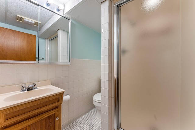 full bathroom featuring a shower stall, tile walls, toilet, tile patterned flooring, and vanity