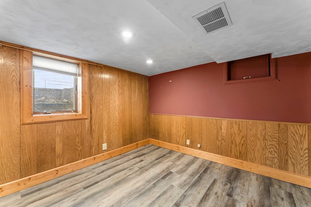 basement featuring wood finished floors, wood walls, baseboards, and recessed lighting