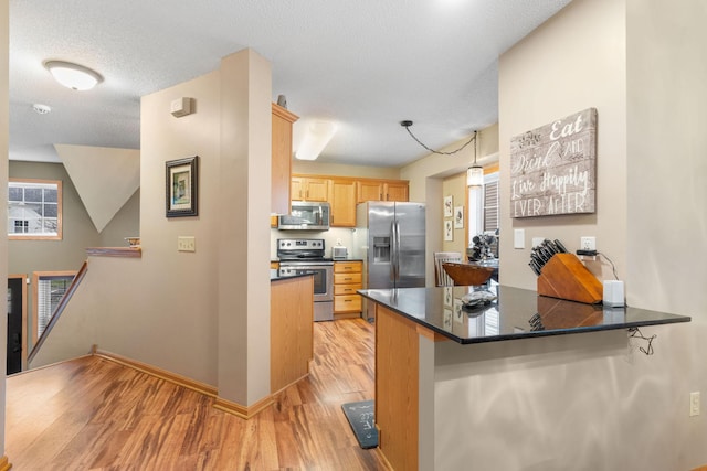 kitchen with a peninsula, dark countertops, stainless steel appliances, and light wood finished floors