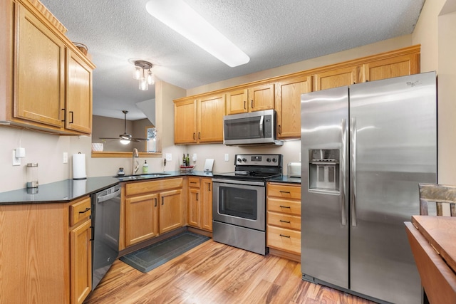 kitchen with dark countertops, a sink, a textured ceiling, light wood-style flooring, and stainless steel appliances
