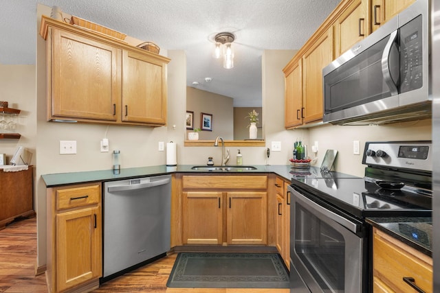 kitchen featuring dark countertops, appliances with stainless steel finishes, a sink, and wood finished floors