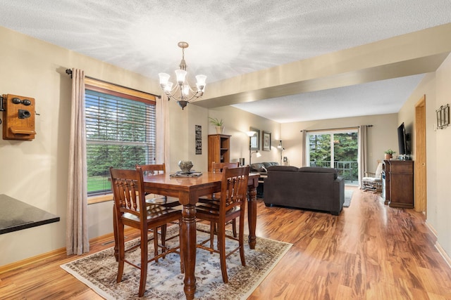 dining space featuring a textured ceiling, baseboards, an inviting chandelier, and light wood finished floors