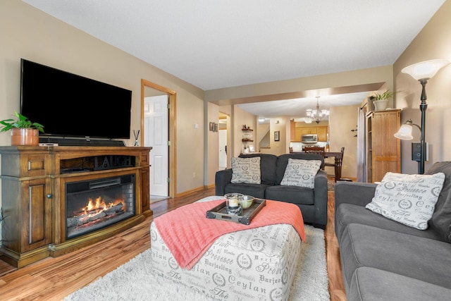 living area featuring a glass covered fireplace, light wood-style flooring, and a notable chandelier
