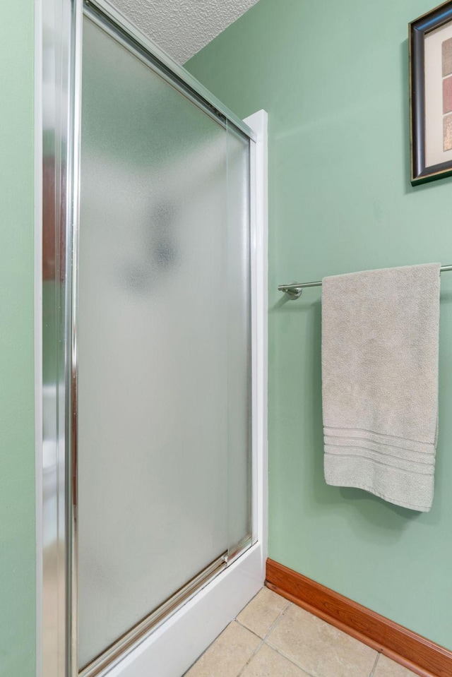 bathroom featuring tile patterned flooring, a textured ceiling, baseboards, and a stall shower