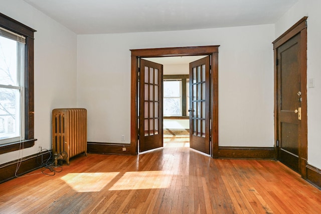 unfurnished room featuring french doors, radiator heating unit, hardwood / wood-style floors, and baseboards