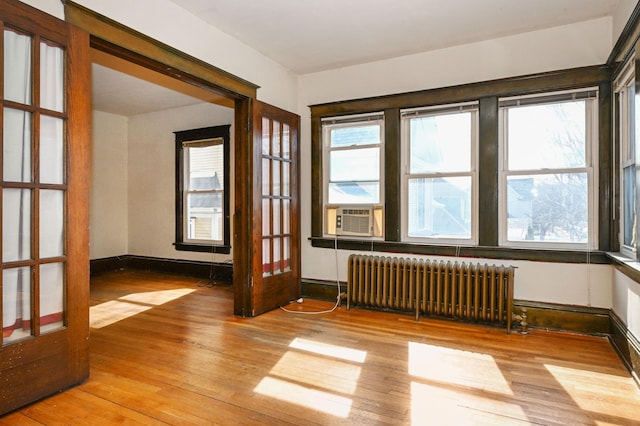 spare room with baseboards, wood-type flooring, radiator, cooling unit, and french doors