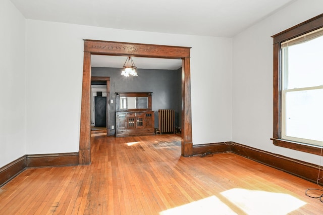 unfurnished room with a notable chandelier, baseboards, hardwood / wood-style floors, and radiator