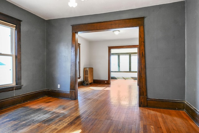 empty room featuring radiator heating unit, hardwood / wood-style floors, and baseboards