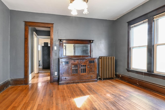 unfurnished living room with a notable chandelier, hardwood / wood-style flooring, baseboards, and radiator
