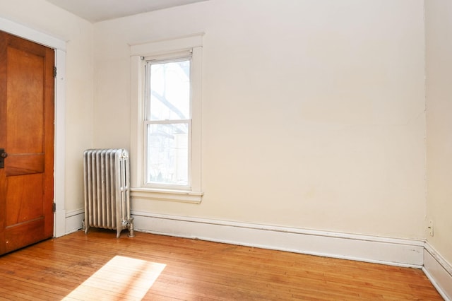empty room featuring radiator heating unit, hardwood / wood-style flooring, and baseboards