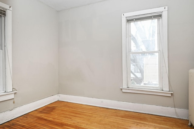 empty room featuring wood finished floors, radiator heating unit, baseboards, and plenty of natural light