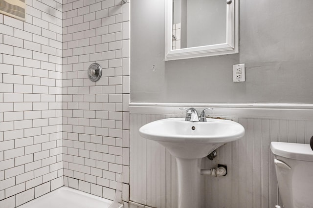 bathroom featuring toilet, a stall shower, a sink, and wainscoting