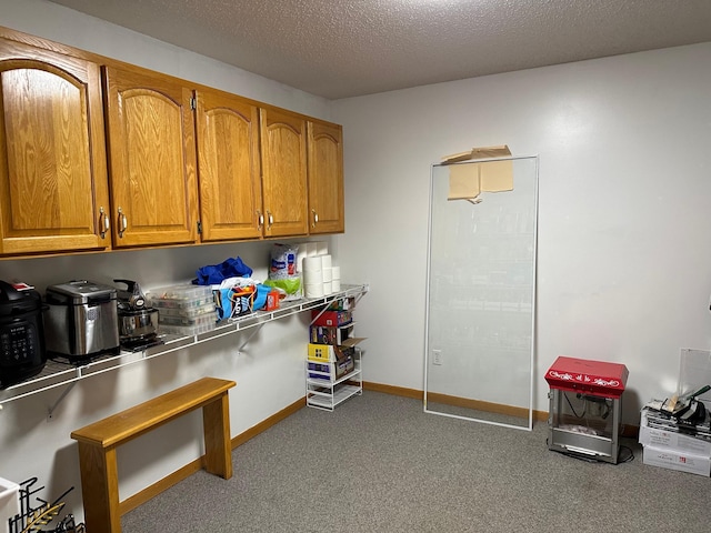 kitchen with brown cabinets, a textured ceiling, carpet flooring, and baseboards