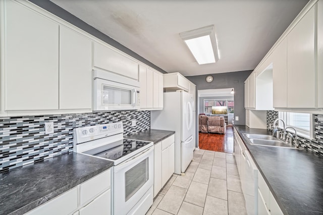 kitchen with a sink, dark countertops, white cabinetry, white appliances, and light tile patterned floors