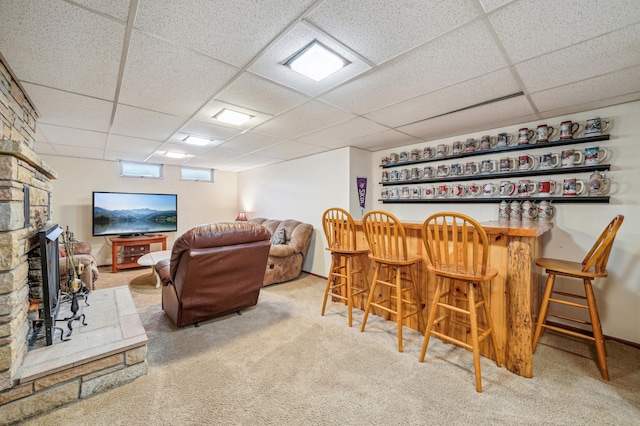 interior space featuring a stone fireplace, carpet flooring, a drop ceiling, and a bar