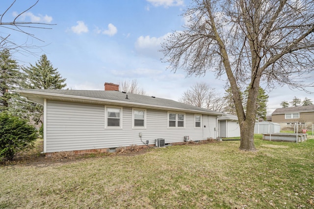 back of property with a chimney, crawl space, central air condition unit, and a lawn