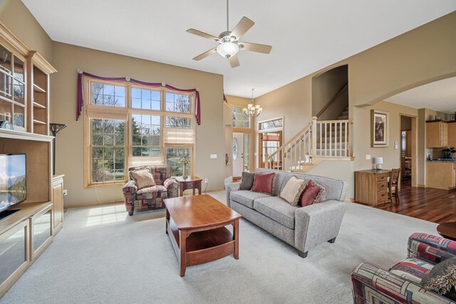 carpeted living room with arched walkways, stairway, a towering ceiling, and ceiling fan with notable chandelier