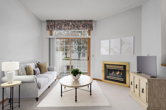 living room with light colored carpet, baseboards, a glass covered fireplace, and a textured ceiling