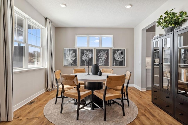 dining room featuring light wood-type flooring, baseboards, visible vents, and a textured ceiling