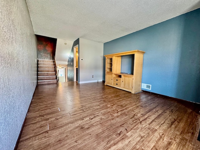 unfurnished living room featuring wood finished floors, a textured ceiling, a textured wall, stairs, and baseboards