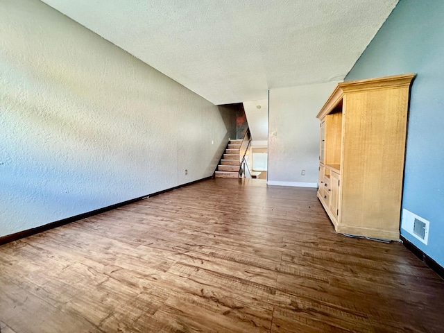 unfurnished living room with stairs, wood finished floors, a textured ceiling, and baseboards